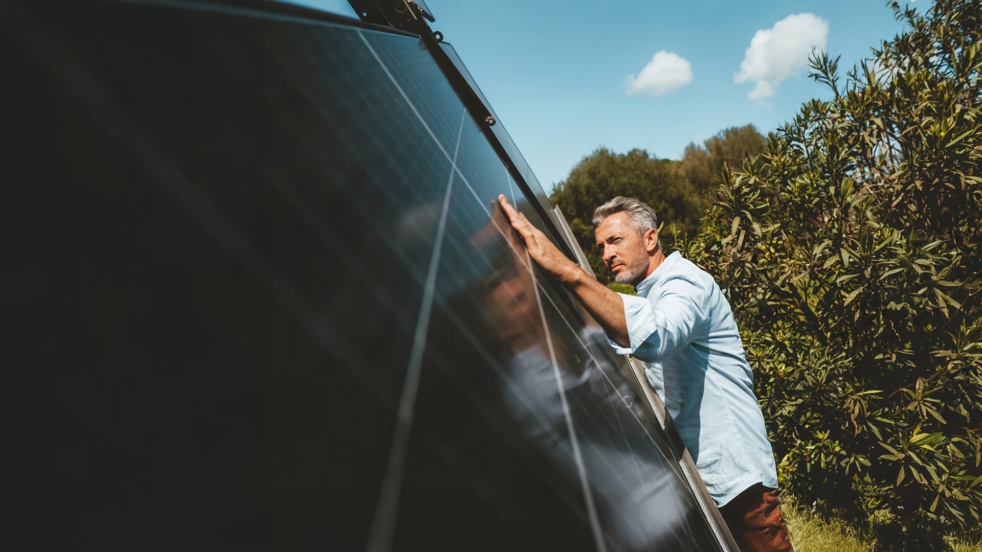 Mann kontrolliert ein Balkonkraftwerk-Solarmodul bei Sonnenschein